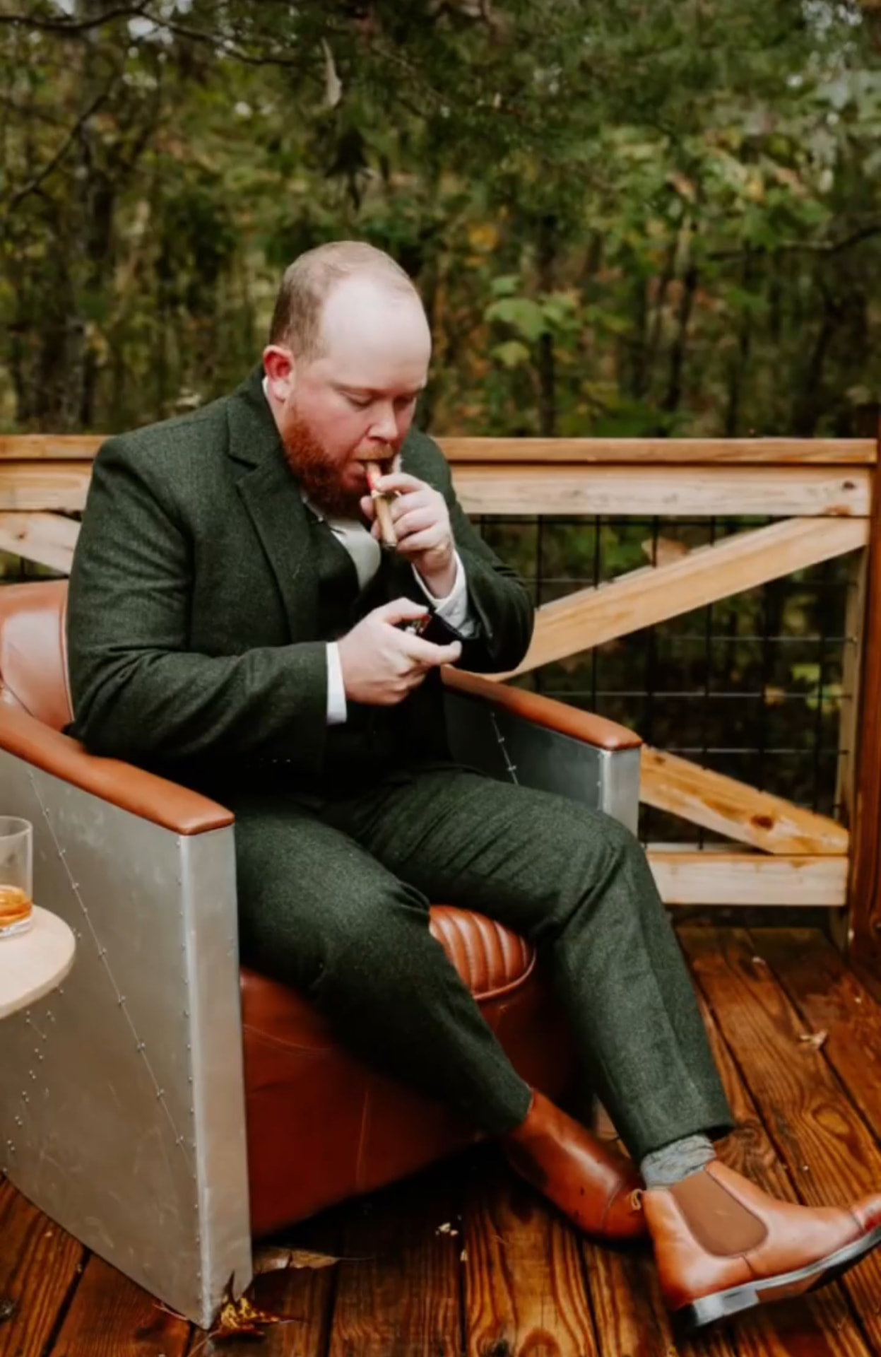 Groom relaxing in a forest green tweed suit with tan leather boots